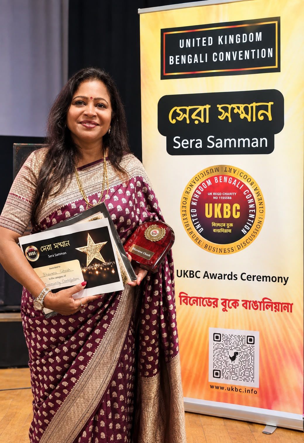 Bhavana Ghosh holding the Sera Samman award beside the United Kingdom Bengali Convention banner